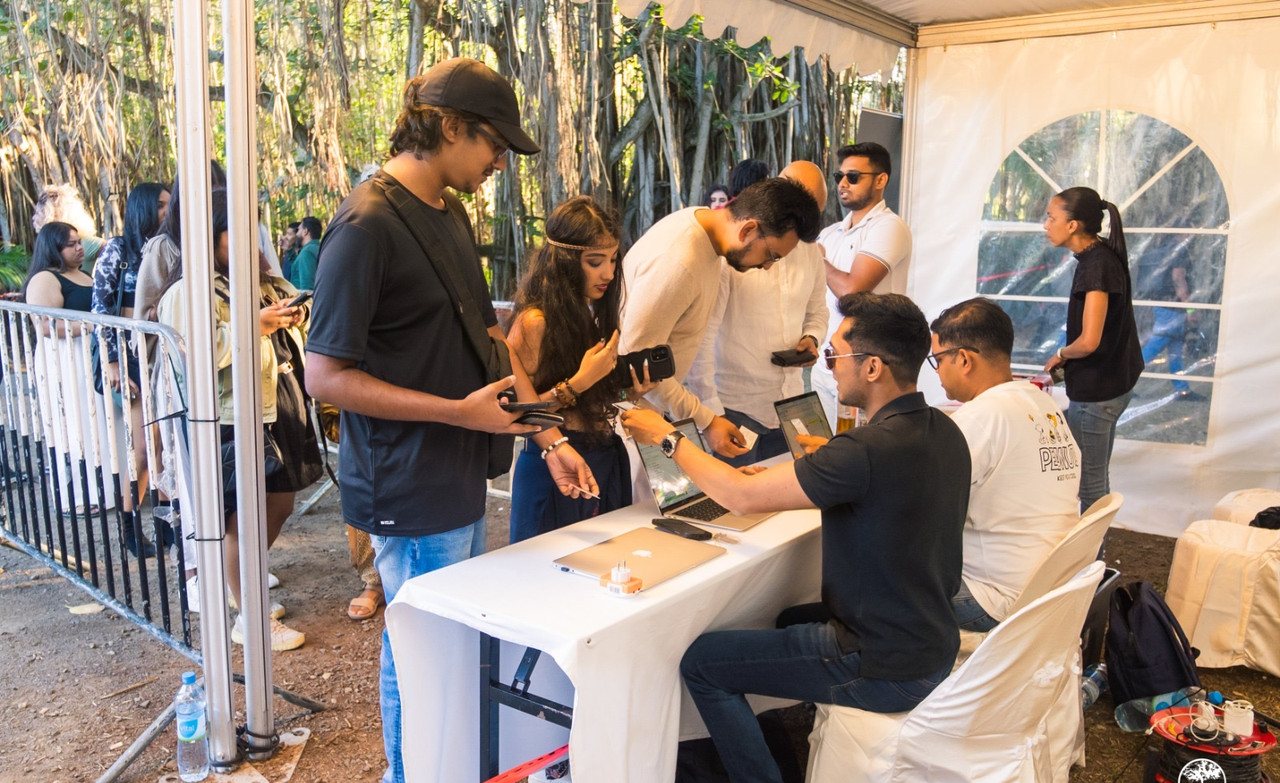 Daytime check-in and ticketing desk under a white marquee, with event staff on laptops greeting attendees queued behind barriers