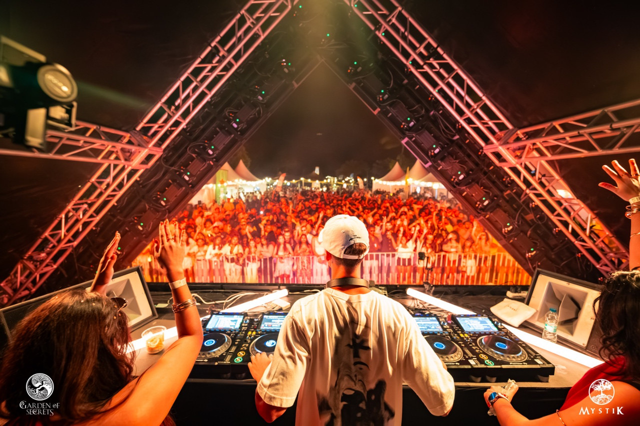 DJ performing from behind a triangular lighting truss to a packed outdoor festival crowd
